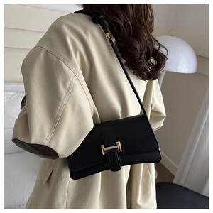 Detailed view of a black matte leather shoulder bag with a square metal buckle on a model