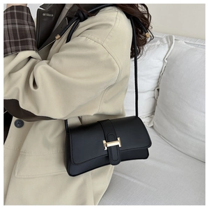 Close-up of black leather underarm bag with gold metal buckle and knotted strap details