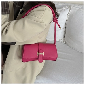 Detail of rose red leather baguette bag with gold buckle on a beige coat outfit