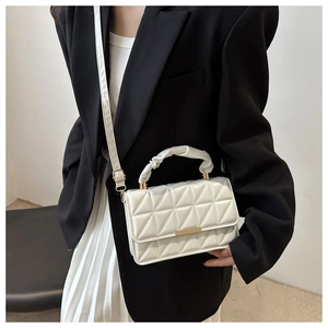 Close-up of a white quilted crossbody bag featuring a unique pleated handle and gold clasp