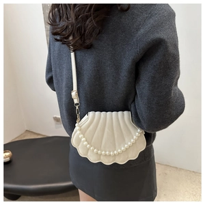 Detail view of cream shell-shaped crossbody bag with pearl chain and adjustable strap