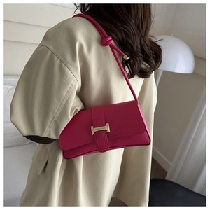 Detail of fuchsia leather bag with gold H-buckle worn over a beige trench coat