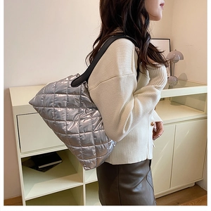 Silver quilted tote bag with metallic finish and black strap shown on a model's shoulder