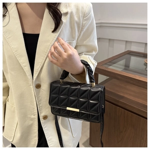 Detail of a black quilted handbag with a gold rectangle lock on a beige blazer