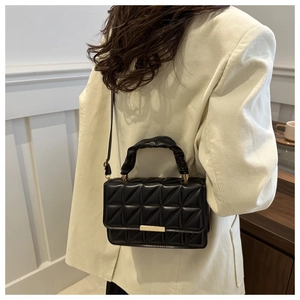 Detail of black quilted leather crossbody bag worn with a white blazer for a minimalist look