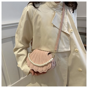 Detail of pink shell-shaped crossbody bag with pearl strap on model in trench coat