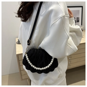 Detail of black velvet shell bag featuring a luxury pearl chain strap on a white sweater