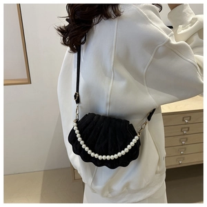 Rear view of model wearing a black shell-shaped crossbody bag with decorative pearl strap