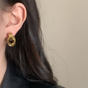Minimalist geometric twisted gold hoop earrings shown on a model with a black jacket