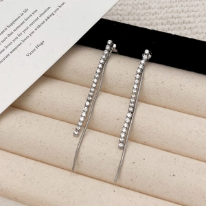 Detailed view of silver tassel earrings with zircon studs on beige velvet jewelry tray
