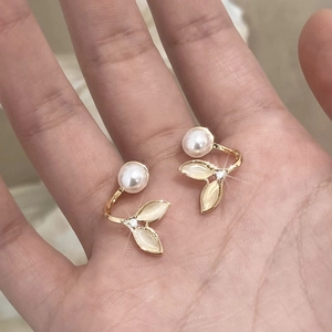 Detailed close-up of golden fishtail earrings with white pearls and cat eye stone inlay