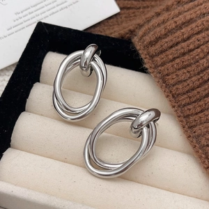 Detail of twisted silver geometric hoop earrings on a beige velvet jewelry tray display