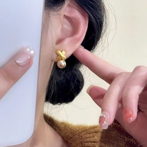 Elegant gold-plated X-shape earrings with a champagne pearl drop on a model