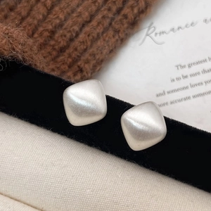 Macro shot of brushed silver square stud earrings on textured fabric and velvet background