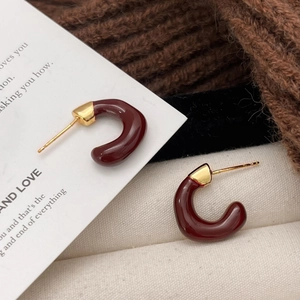 Elegant C-shaped burgundy enamel earrings with gold metal caps on a cozy knit background