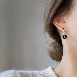 Elegant gold hoop earrings with black square pendant on model against gray background