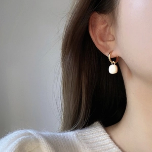 Detail view of a gold round metal earring with a square cream resin drop on a model
