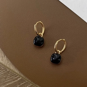 Minimalist gold hoop earrings with black square pendant on textured leather background