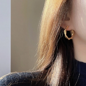 Close-up of golden spiral twisted hoop earring showing delicate metal texture and shine