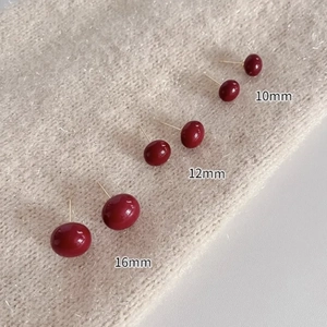 Red pearl stud earrings in 10mm, 12mm and 16mm sizes on a soft beige knit fabric