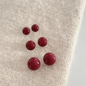 Three pairs of glossy red bead earrings in different sizes on beige knit fabric