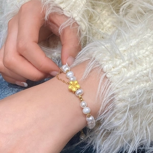 Natural freshwater pearl bracelet with golden peach blossom charm worn on a female wrist