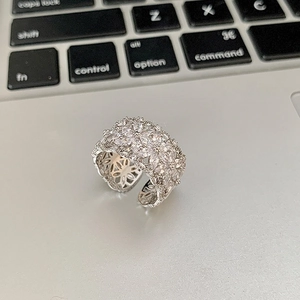 Détail macro d'une bague ouverte argentée ornée de motifs de fleurs en zircons brillants