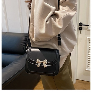 Detail of black crossbody bag featuring a golden bow buckle and matte leather texture