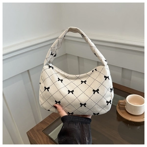 Detail of corduroy texture and black bow embroidery on a cream quilted hobo bag