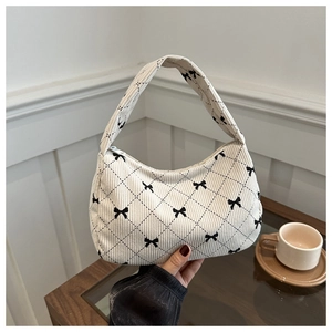 Close-up of quilted beige corduroy handbag featuring black bow patterns and soft texture