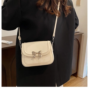 Detail of cream-colored crossbody bag featuring a delicate silver metallic bow accent