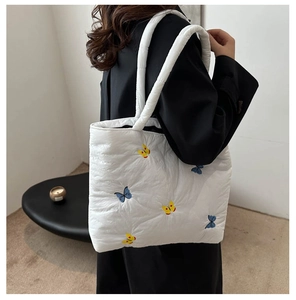 Detailed embroidery of blue and yellow butterflies on a white quilted puffer tote bag
