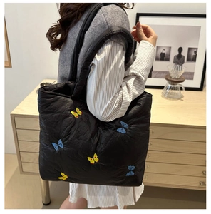 Detail of black quilted tote bag featuring vibrant butterfly embroidery and soft texture