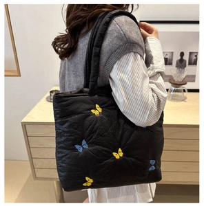 Detail of black quilted tote bag featuring vibrant butterfly embroidery and soft texture
