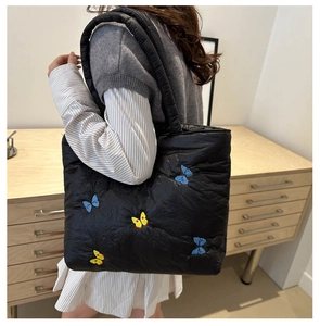 Detail of a black quilted tote bag with colorful butterfly embroidery and soft texture