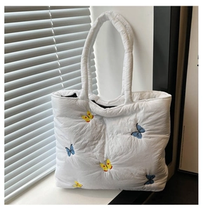 Detail of white quilted tote bag featuring vibrant blue and yellow butterfly embroidery