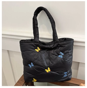 Close-up of black quilted tote bag featuring vibrant butterfly embroidery and soft padded handles