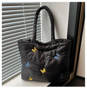 Close-up of quilted butterfly embroidery on a black shoulder tote bag with fine stitching