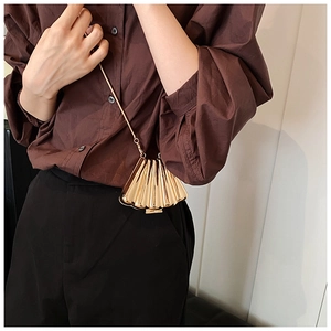 Detail of shell-shaped gold metal clutch bag with chain strap worn by a fashion model