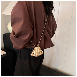 Detail of a golden shell-shaped clutch with metallic texture and thin chain strap on a model