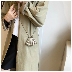 Detail of silver shell-shaped mini clutch with chain strap on a khaki trench coat