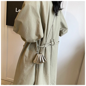 Silver shell-shaped metallic mini bag with chain strap worn over a stylish trench coat