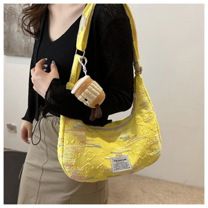 Dettaglio ricamo su borsa a mezzaluna gialla con etichetta Fashion Instinct e ciondolo
