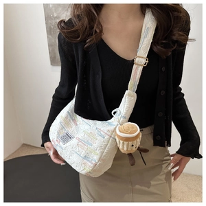 Detail of white quilted crossbody bag with colorful embroidery and coffee cup plush charm