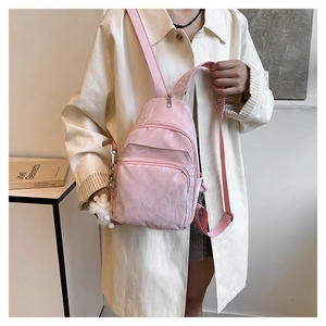 Detail of pink mini chest bag featuring glossy wrinkled texture and white pompom charm