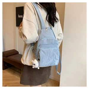 Close-up of light blue pleated nylon chest bag with functional pockets and plush ball charm