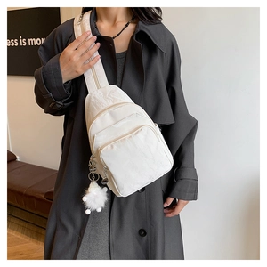 Close-up of white textured crossbody bag featuring pleated fabric and plush ball charm