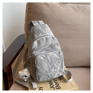 Detail of silver pleated crossbody bag with metal zippers and plush toy pendant charm