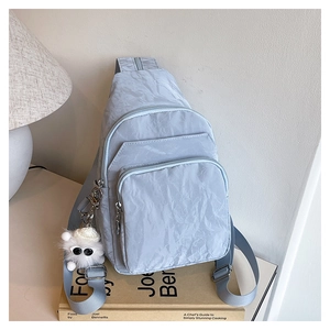 Detail of light blue nylon sling bag with crinkle texture and white plush monster charm