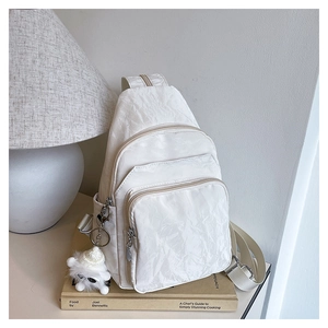 Detail of white wrinkled texture backpack with zipper pockets and plush monster charm